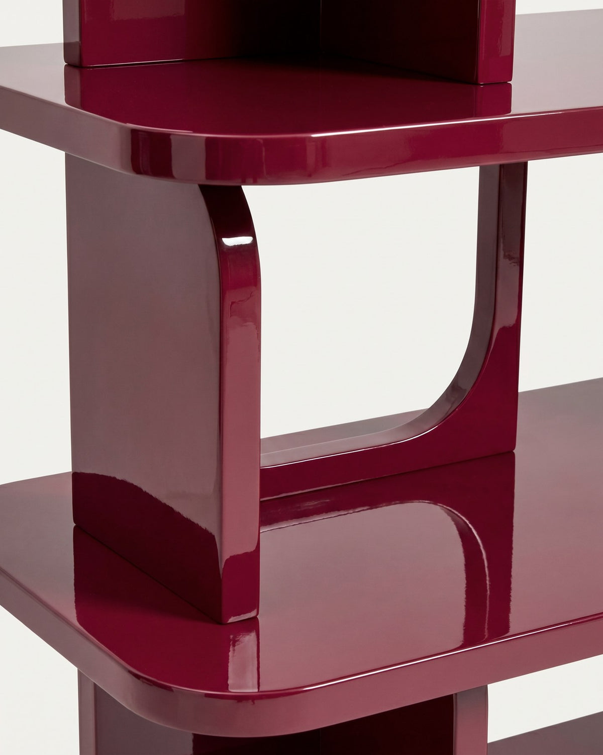 Freistehendes Regal aus MDF und Buchenholz in glänzendem Granatrot, mit geometrischen Aussparungen und mehreren übereinander liegenden Ablageflächen.
