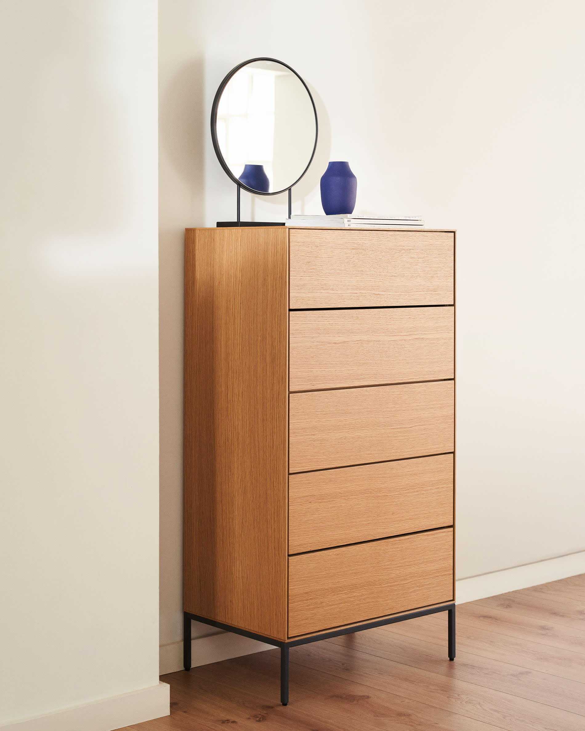 Die Vedrana Kommode kombiniert Eichenfurnier mit schwarzen Stahlbeinen, bietet 5 Schubladen und misst 60 x 114 cm – stilvoll und funktional.