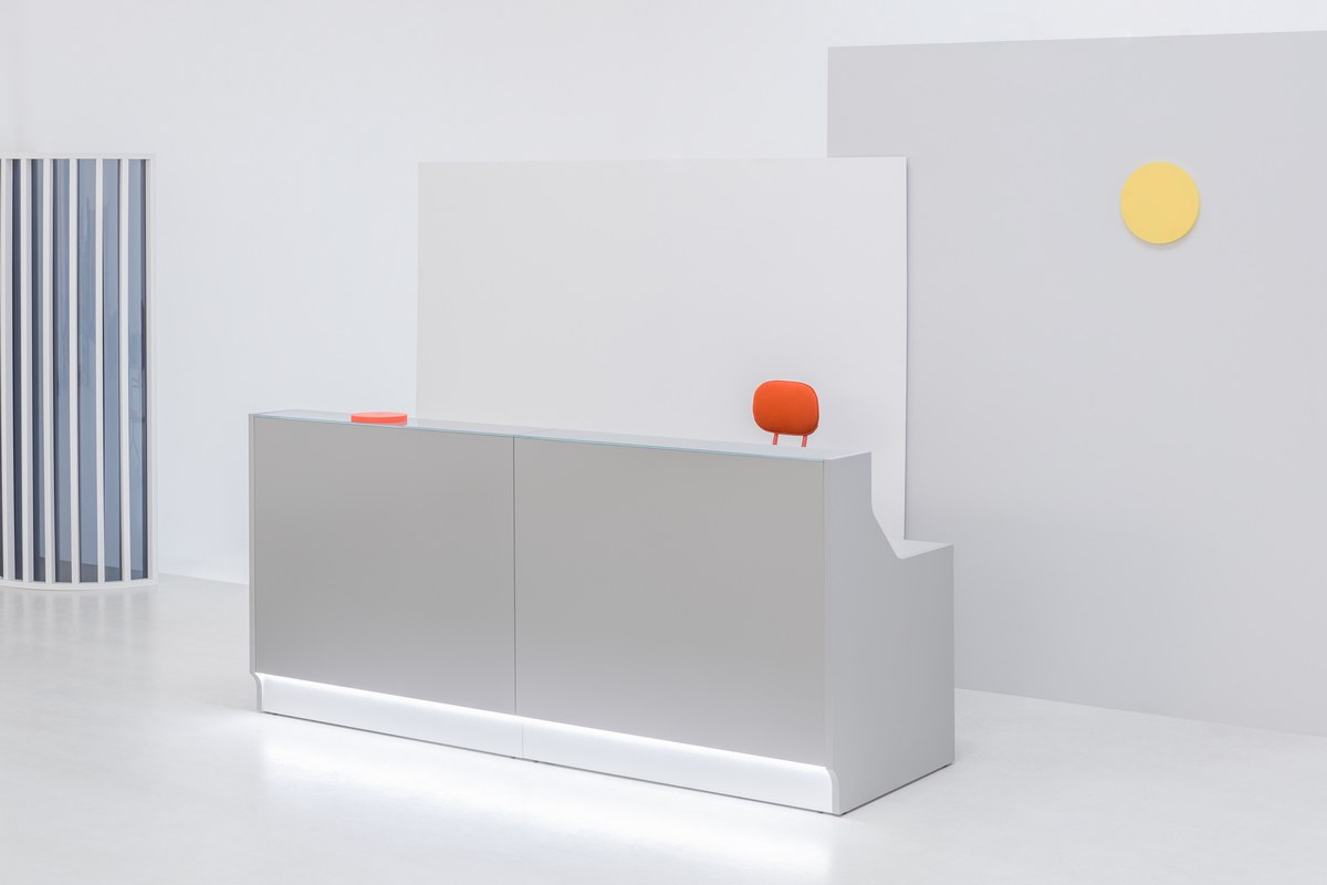 Empfangstheke Linea von Mdd mit silberner Glasfront, gebürstetem Aluminiumsockel und Edelstahl-Eckleiste, LED-Beleuchtung entlang der Theke.