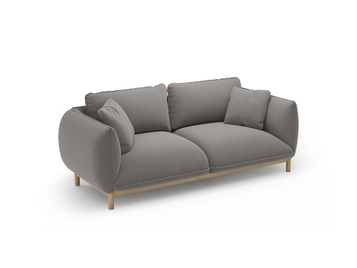 Ada 2er Sofa von Micadoni in Mandel beige mit gepolstertem Velours-Bezug, geschwungener Rückenlehne und sichtbaren Buchenholzbeinen.
