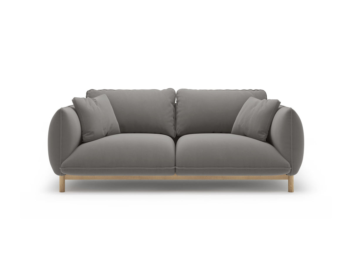 Ada 2er Sofa von Micadoni in Mandel beige mit gepolstertem Velours-Bezug, geschwungener Rückenlehne und sichtbaren Buchenholzbeinen.