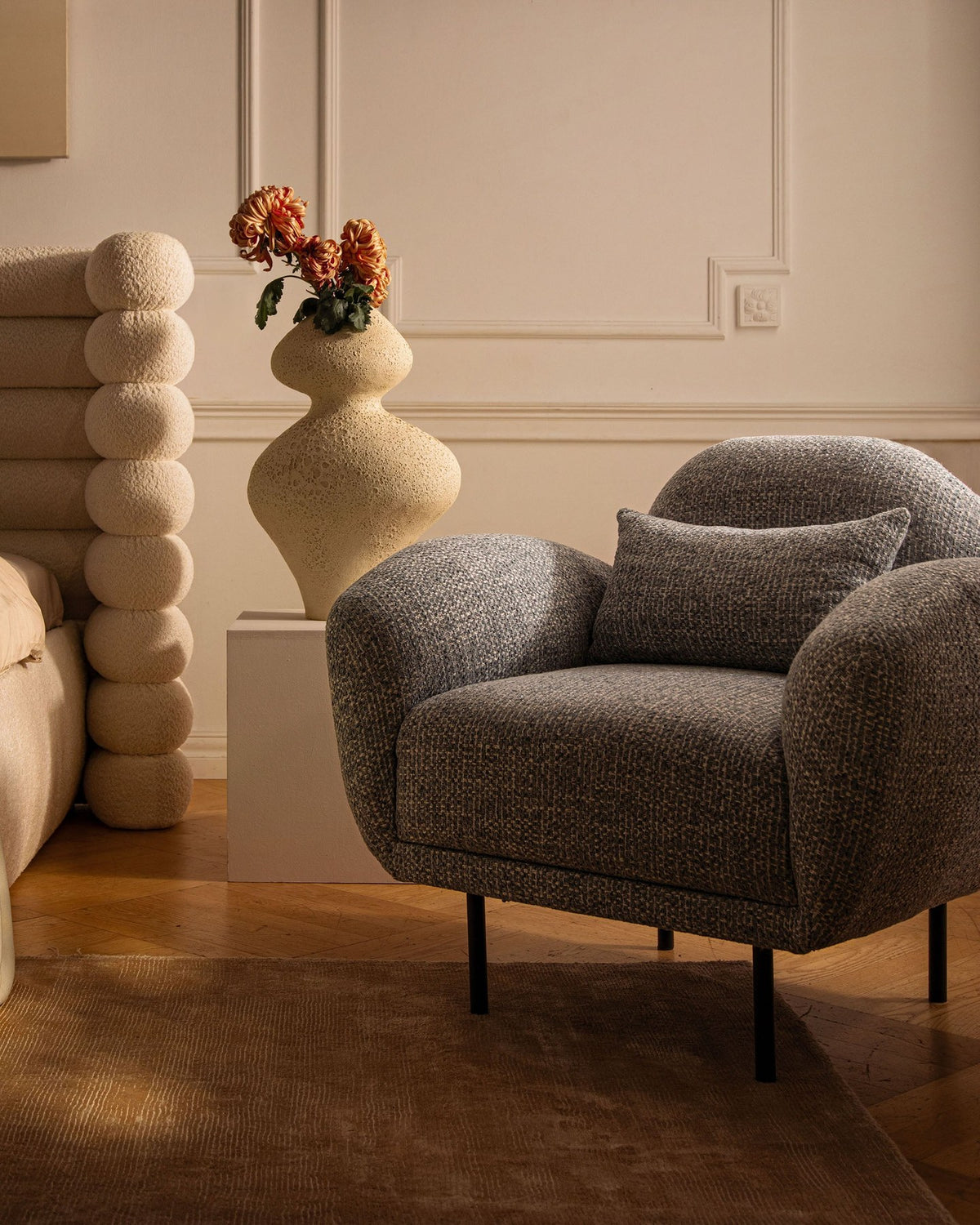 Weisser Poppy Armsessel von Micadoni mit Bouclé-Stoff, abgerundeter Form und schwarzen Metallbeinen, freigestellt fotografiert.