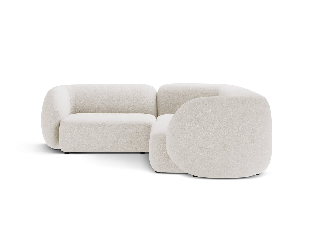 Weisses Ecksofa links Kate von Micadoni mit Bouclé-Stoff Baloo, schwarzen Kunststoffbeinen und niedriger Rückenlehne im Wohnraum.