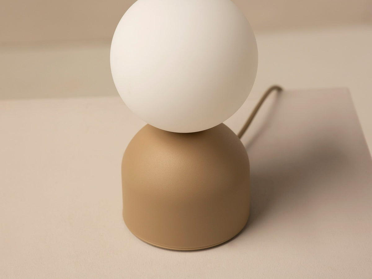 Tischlampe Ely von Micadoni mit rundem Metallfuss und mattem Glasschirm in Beige, Höhe 21 cm, Breite und Tiefe je 12 cm.