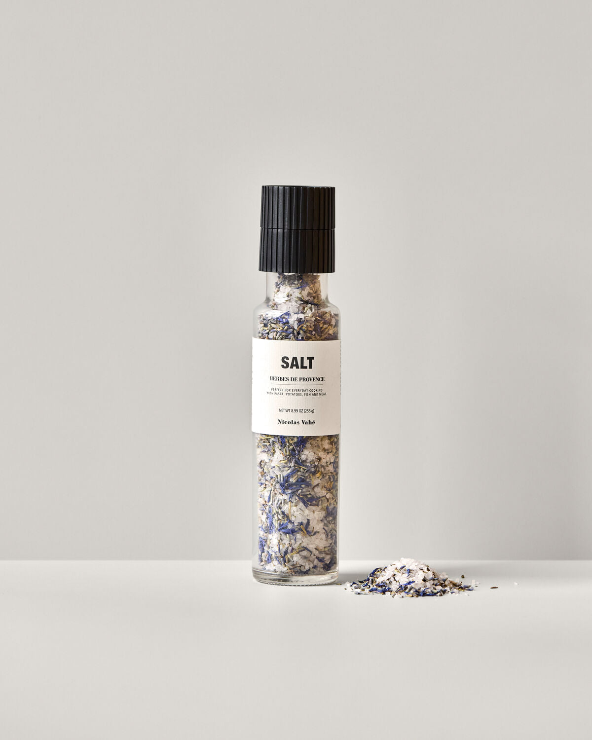 Ein Glas mit Salz und Herbes de Provence von Nicolas Vahé, ideal zum Würzen von Gerichten, stilvoll präsentiert auf einem Holzuntergrund.