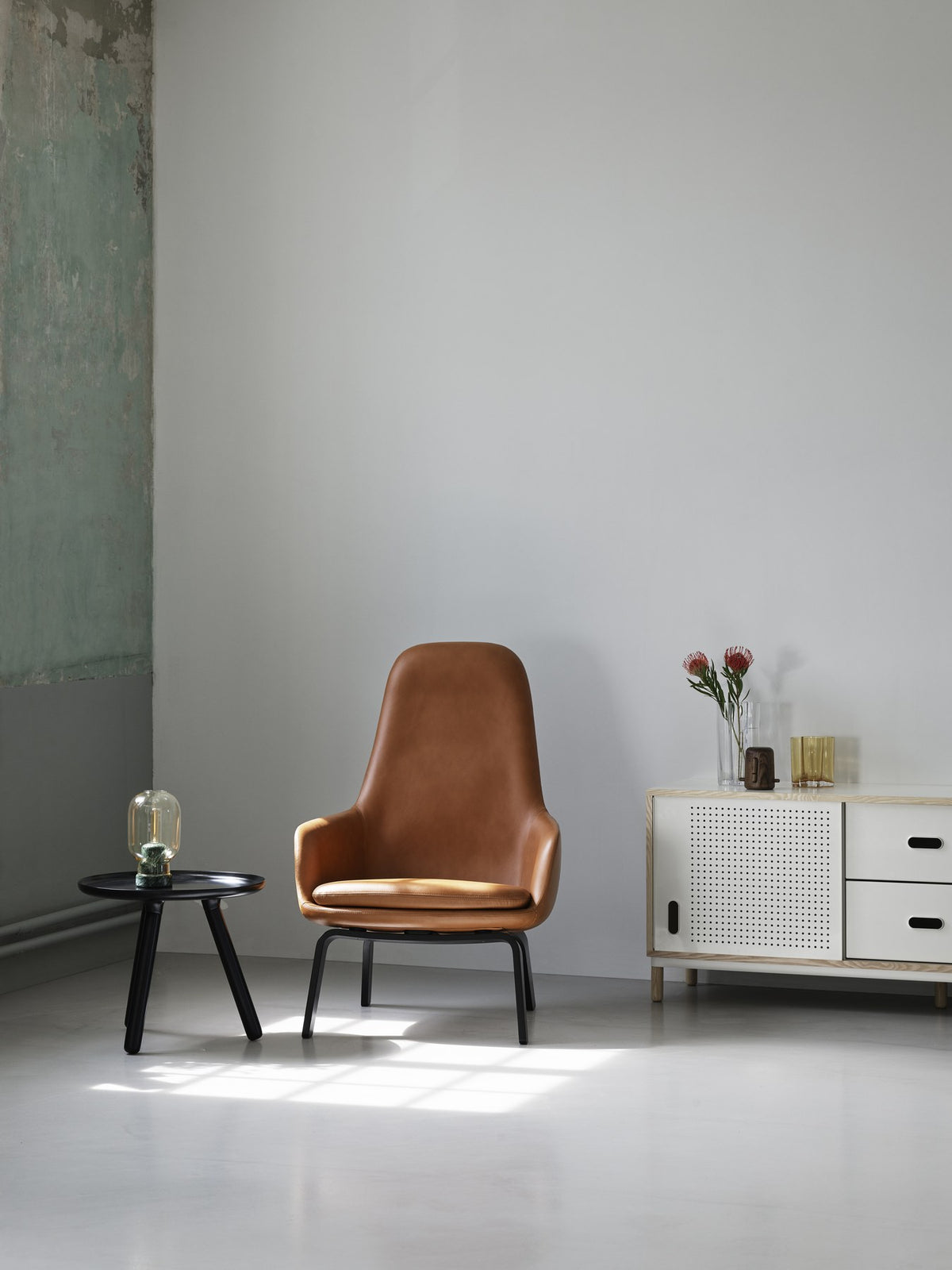 Era Lounge-Sessel hoch mit Stahlgestell, Farbe Cognac, geschwungene Sitzschale mit gepolstertem Kissen und schwarzen Stahlbeinen von Normann Copenhagen.