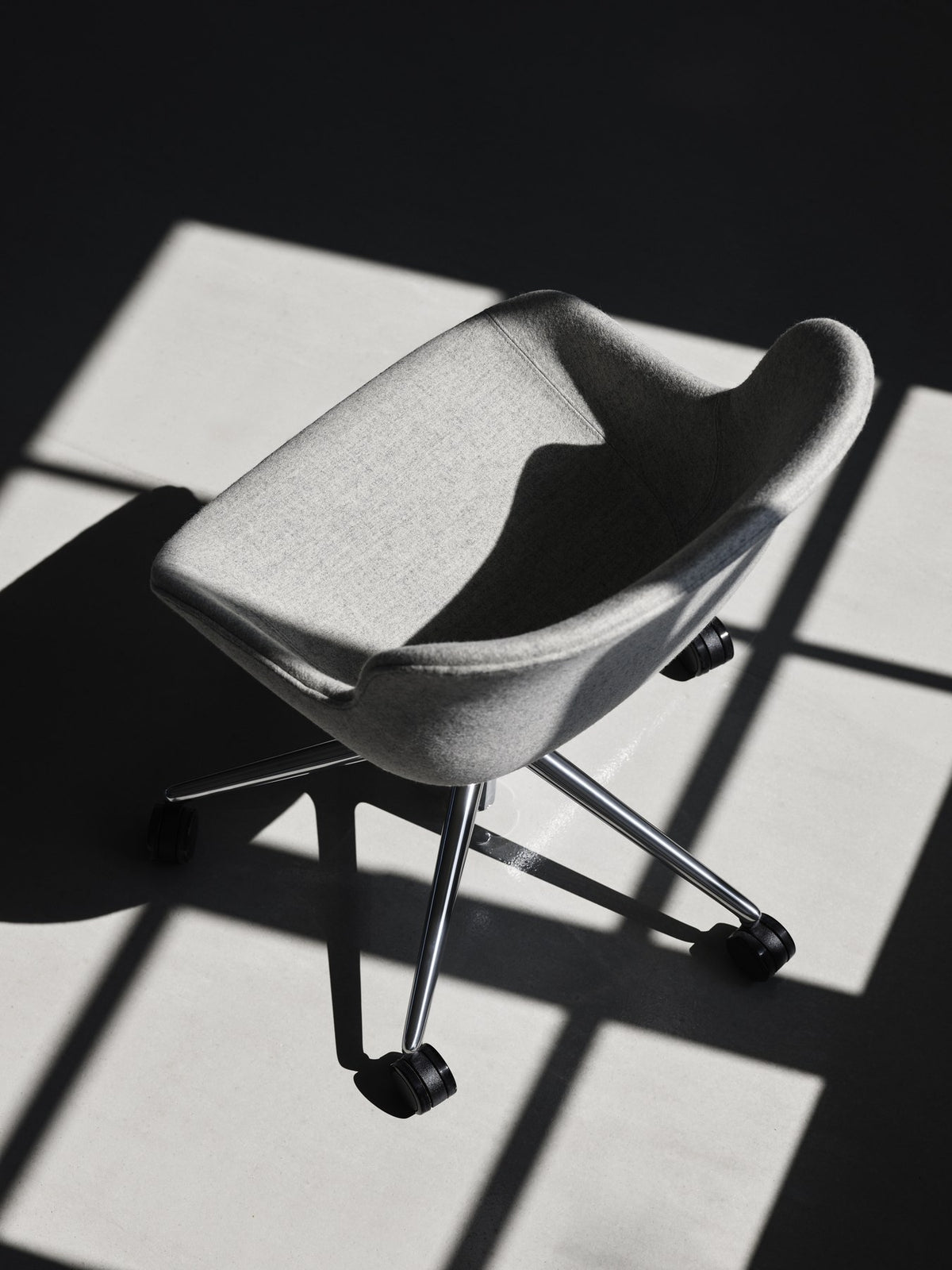 Grauer Hyg Comfort Drehsessel von Normann Copenhagen mit gepolsterter Schale, Aluminiumgestell und fünf Rollen auf drehbarem Fusskreuz.