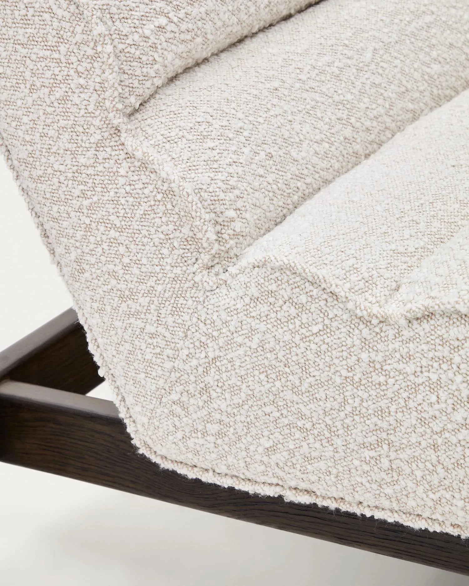 Der Sessel Magira vereint weißes Bouclé mit dunklem Eichenholz, bietet luxuriösen Komfort und ist ein stilvoller Blickfang.