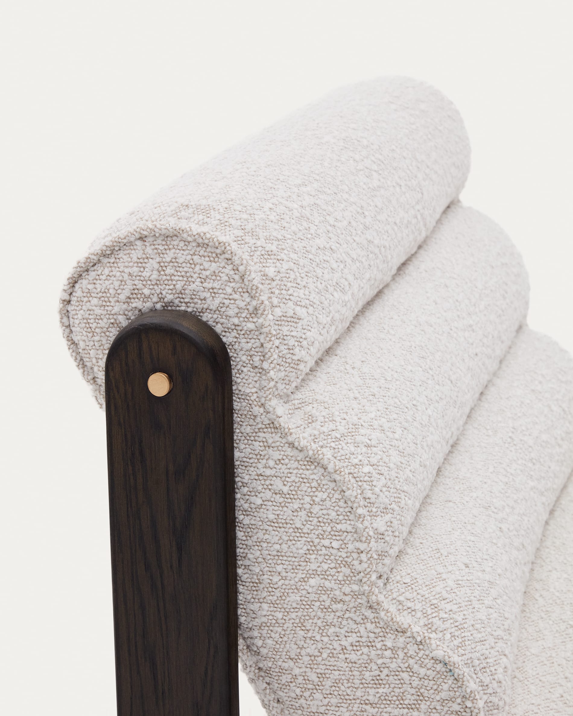 Der Sessel Magira kombiniert weißen Bouclé-Stoff mit dunklem Eichenholz, ideal für stilvolle und zeitgemäße Wohnräume.