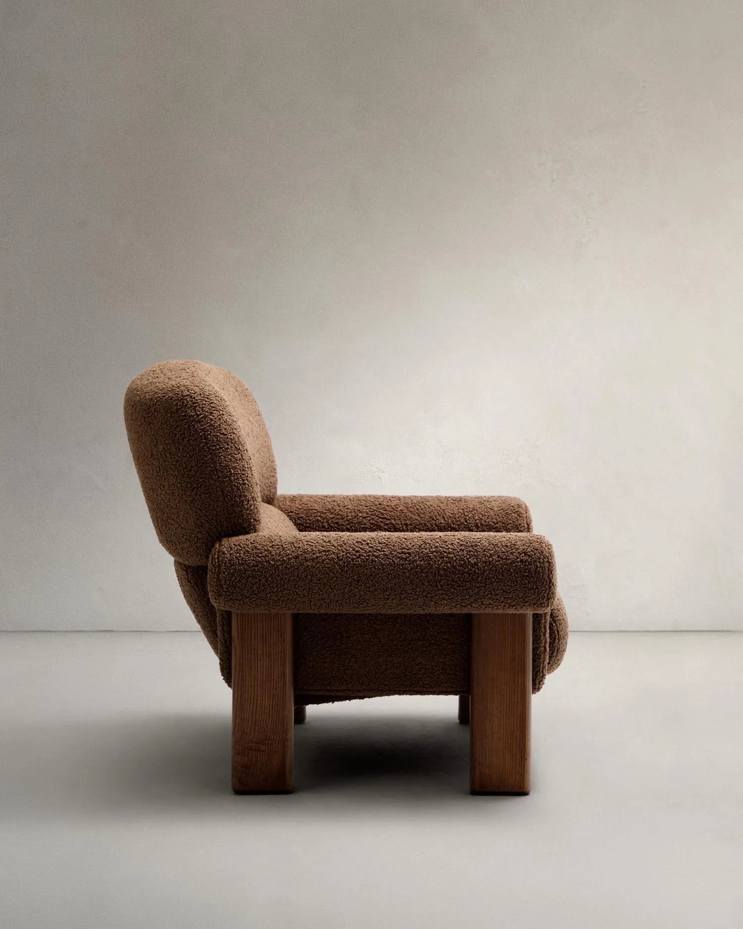 Der Sessel Nema kombiniert taupefarbenes Bouclé mit massivem Eschenholz, bietet luxuriösen Komfort und zeitlose Eleganz.