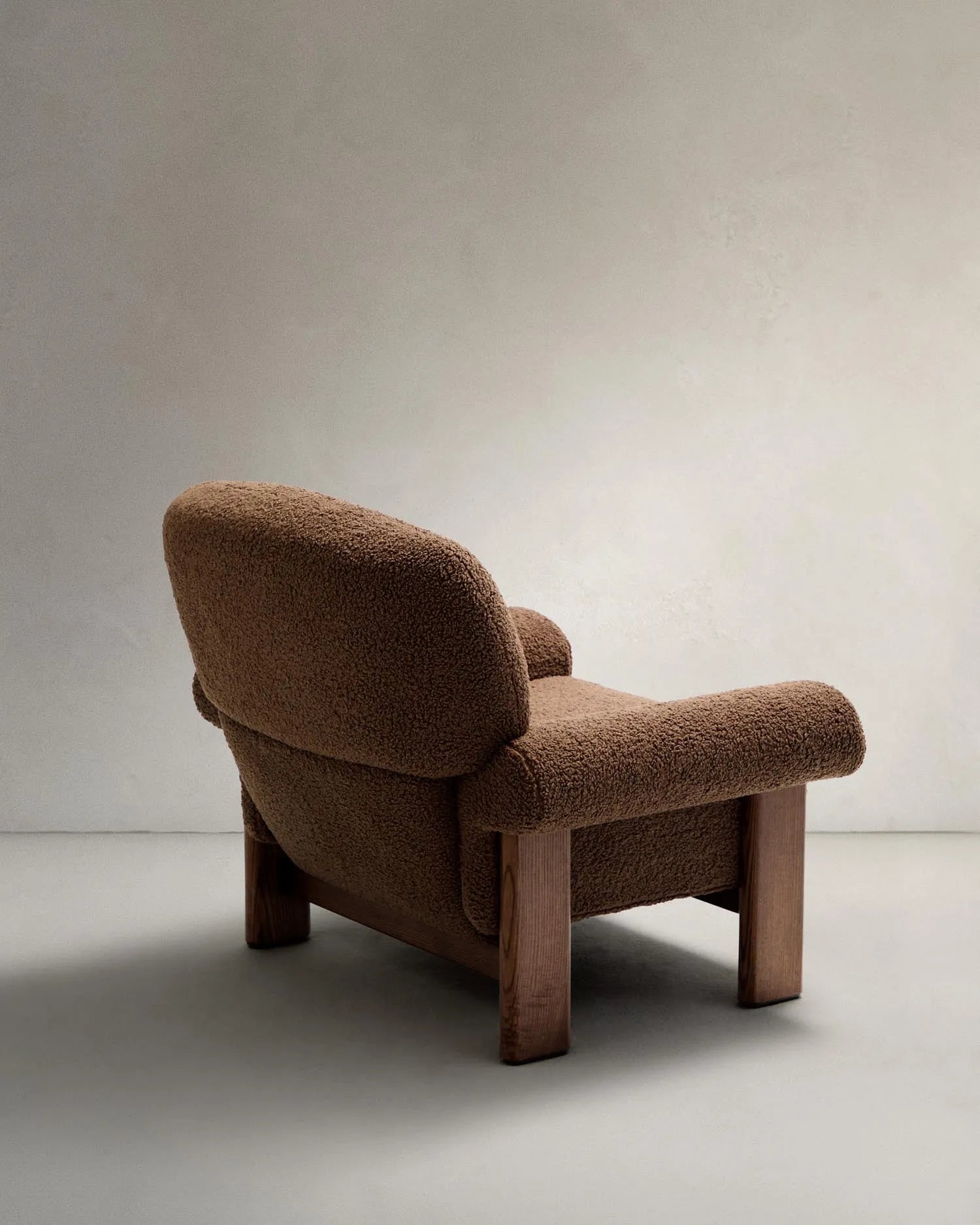 Der Sessel Nema kombiniert taupefarbenes Bouclé mit massivem Eschenholz, bietet luxuriösen Komfort und zeitlose Eleganz.