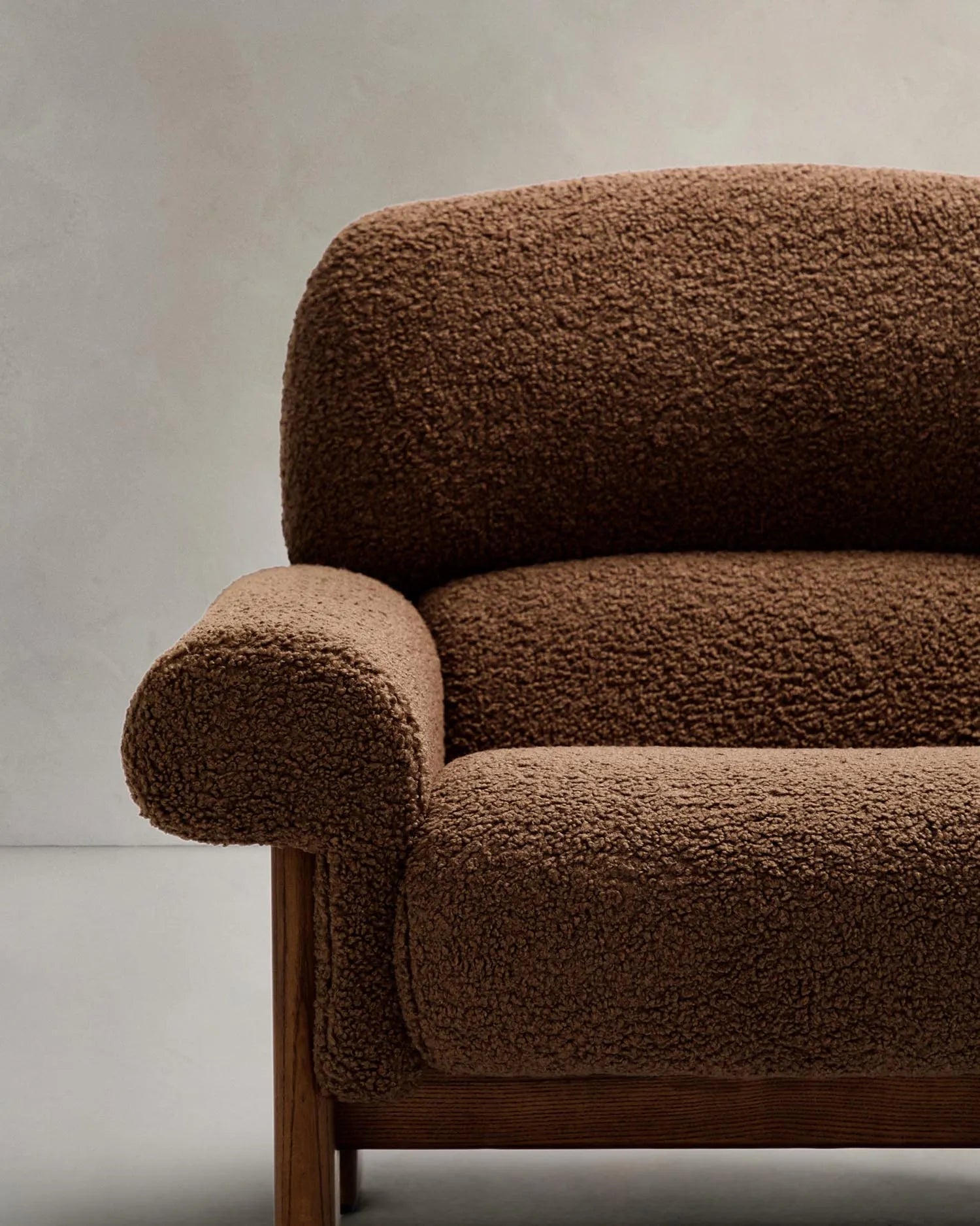 Der Sessel Nema kombiniert taupefarbenes Bouclé mit massivem Eschenholz, bietet luxuriösen Komfort und zeitlose Eleganz.