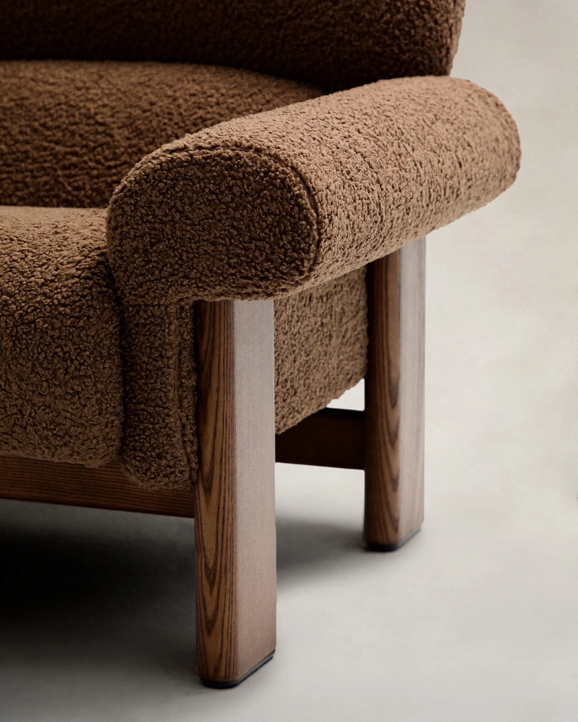 Der Sessel Nema kombiniert taupefarbenes Bouclé mit massivem Eschenholz, bietet luxuriösen Komfort und zeitlose Eleganz.
