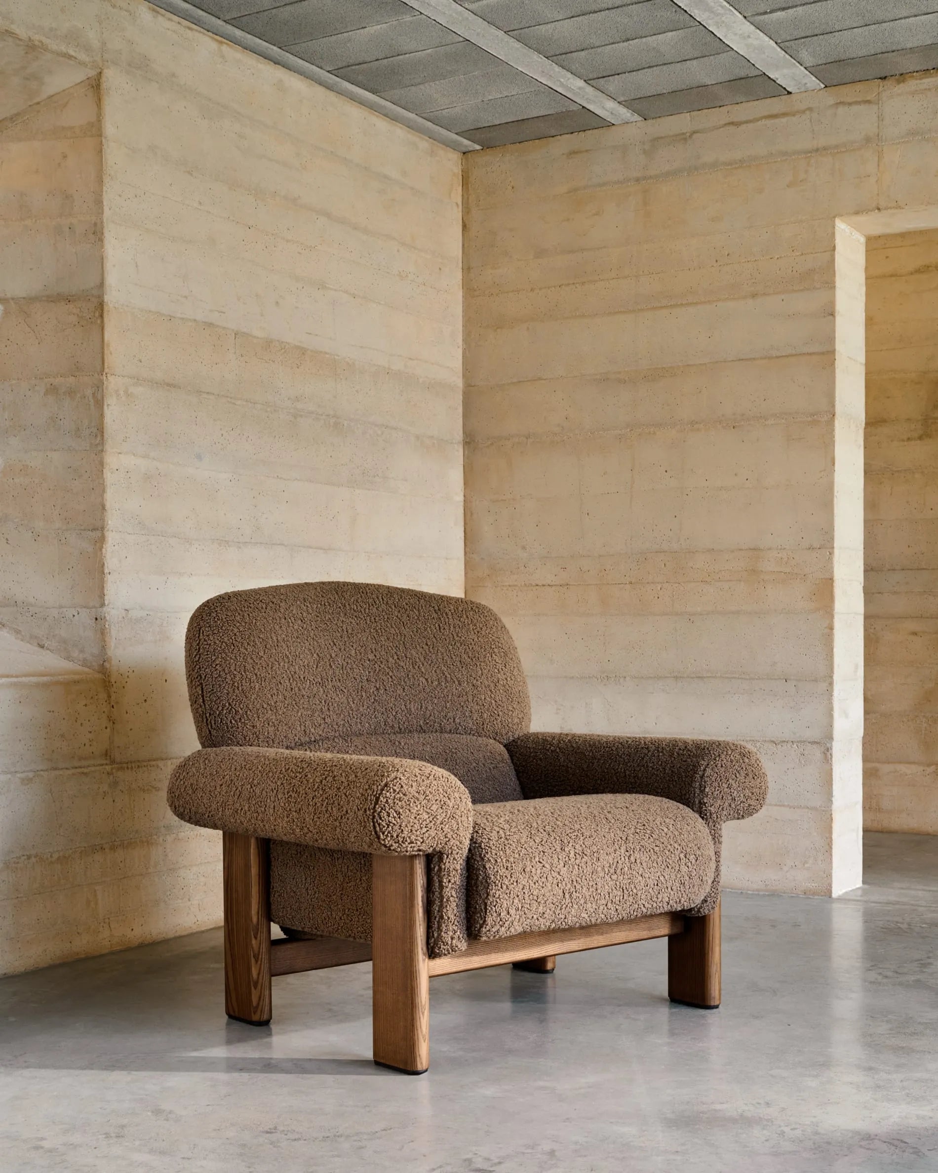 Der Sessel Nema kombiniert taupefarbenes Bouclé mit massivem Eschenholz, bietet luxuriösen Komfort und zeitlose Eleganz.