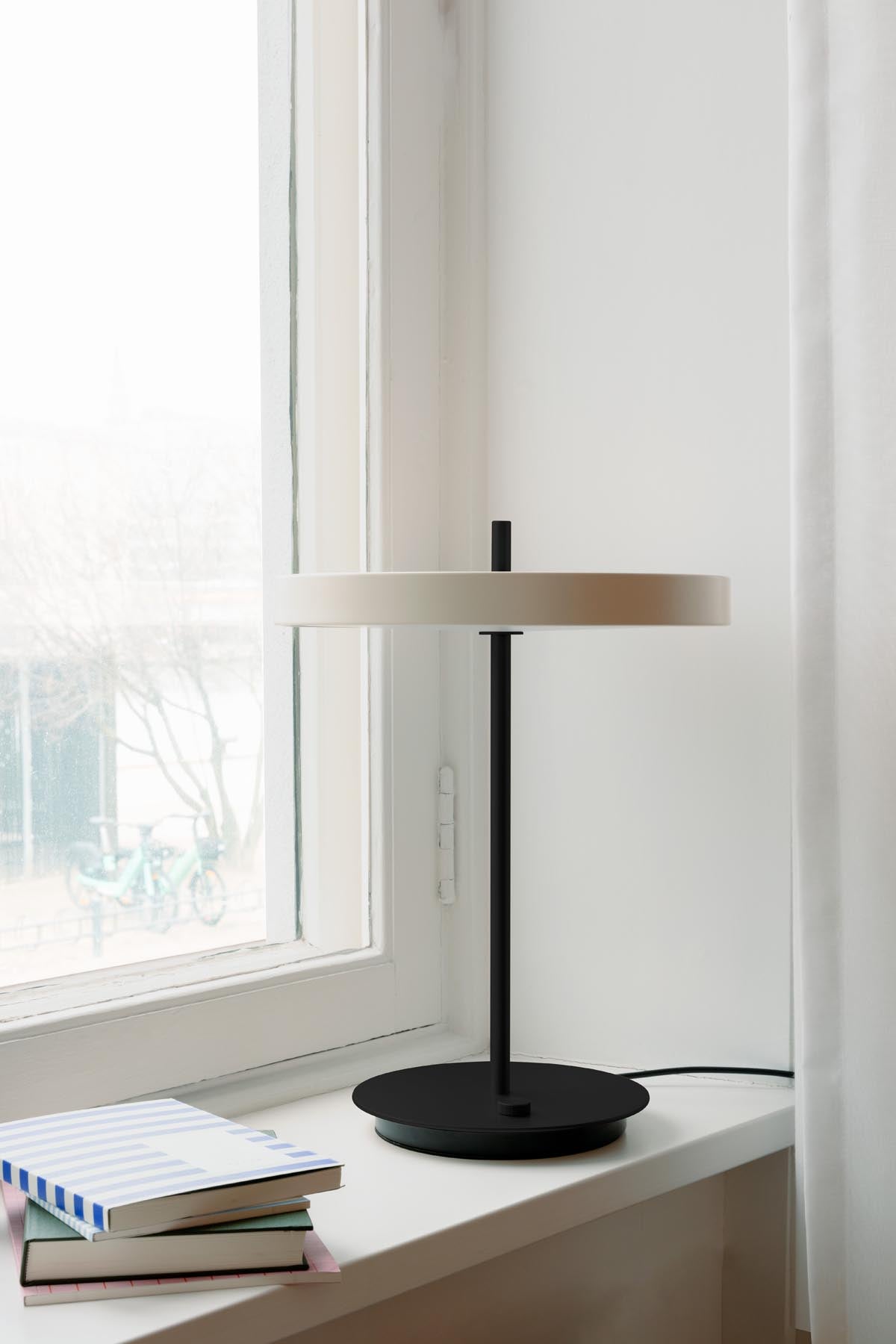 Elegante Asteria Tischleuchte in zartem Pearl White mit schwarzem Sockel, ideal für eine moderne und stilvolle Inneneinrichtung.