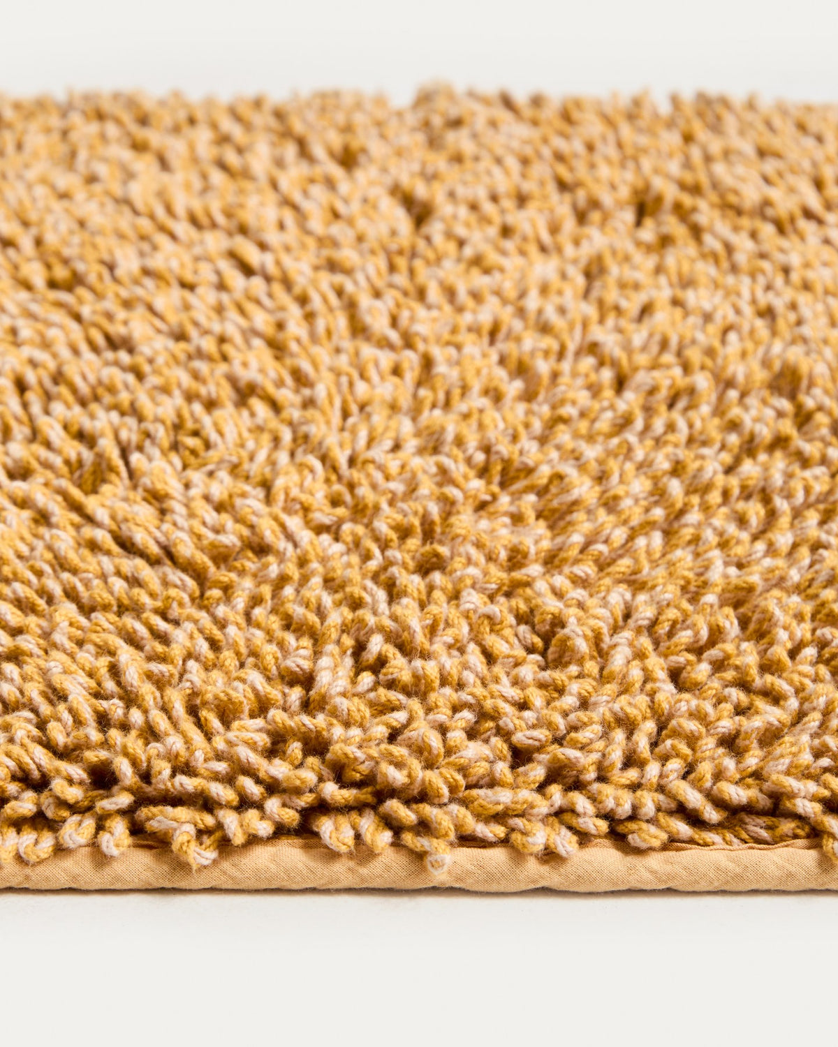 Senfgelbe Badezimmermatte Aroia von Kave Home mit Bouclé-Melange-Struktur in rechteckiger Form, Grösse 50 x 70 cm, auf Boden liegend.