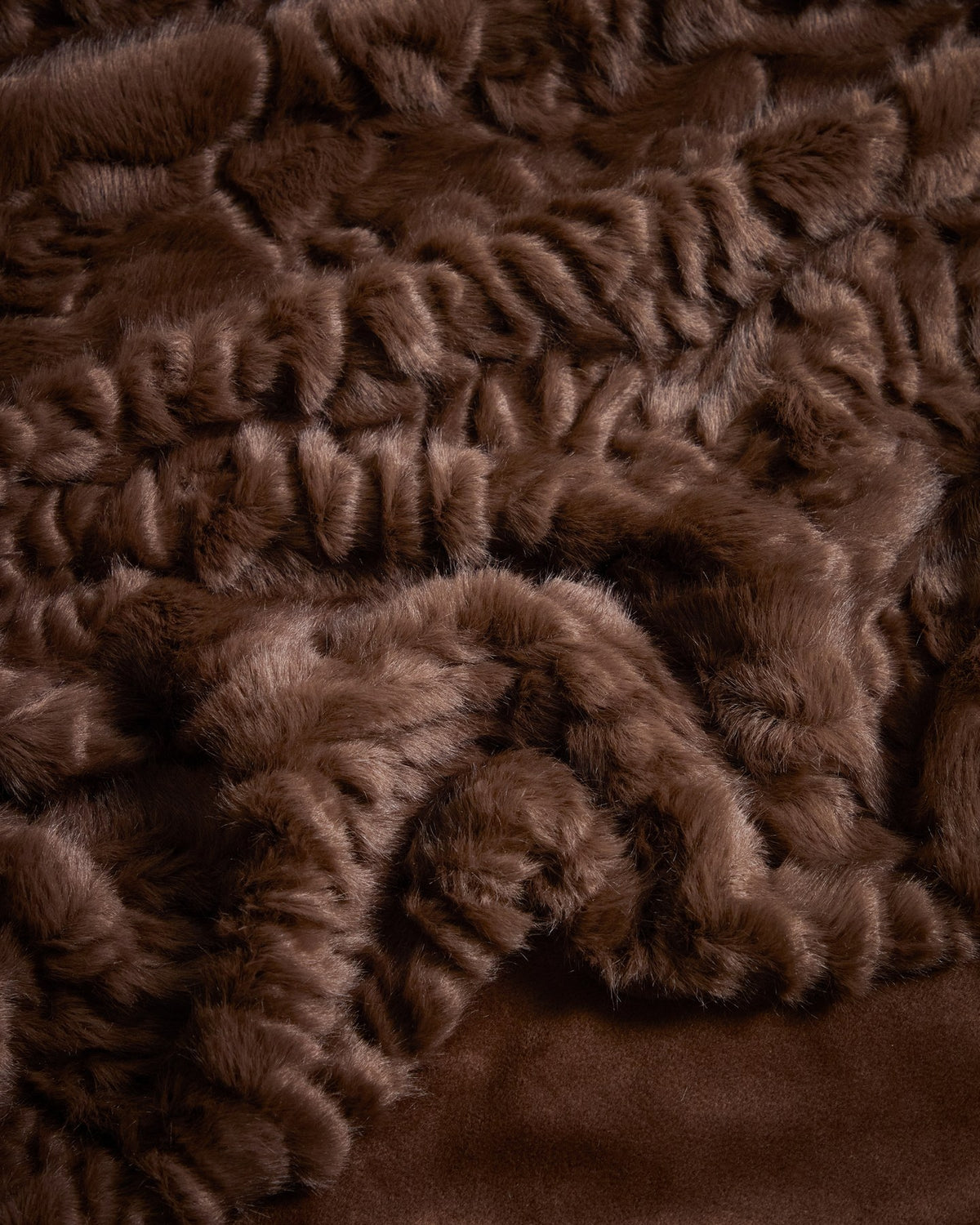 Foto einer schokobraunen Kunstfelldecke mit Astrachan-Optik, Grösse 140 x 200 cm, mit strukturierter, flauschiger Oberfläche und Aufbewahrungsgurt.