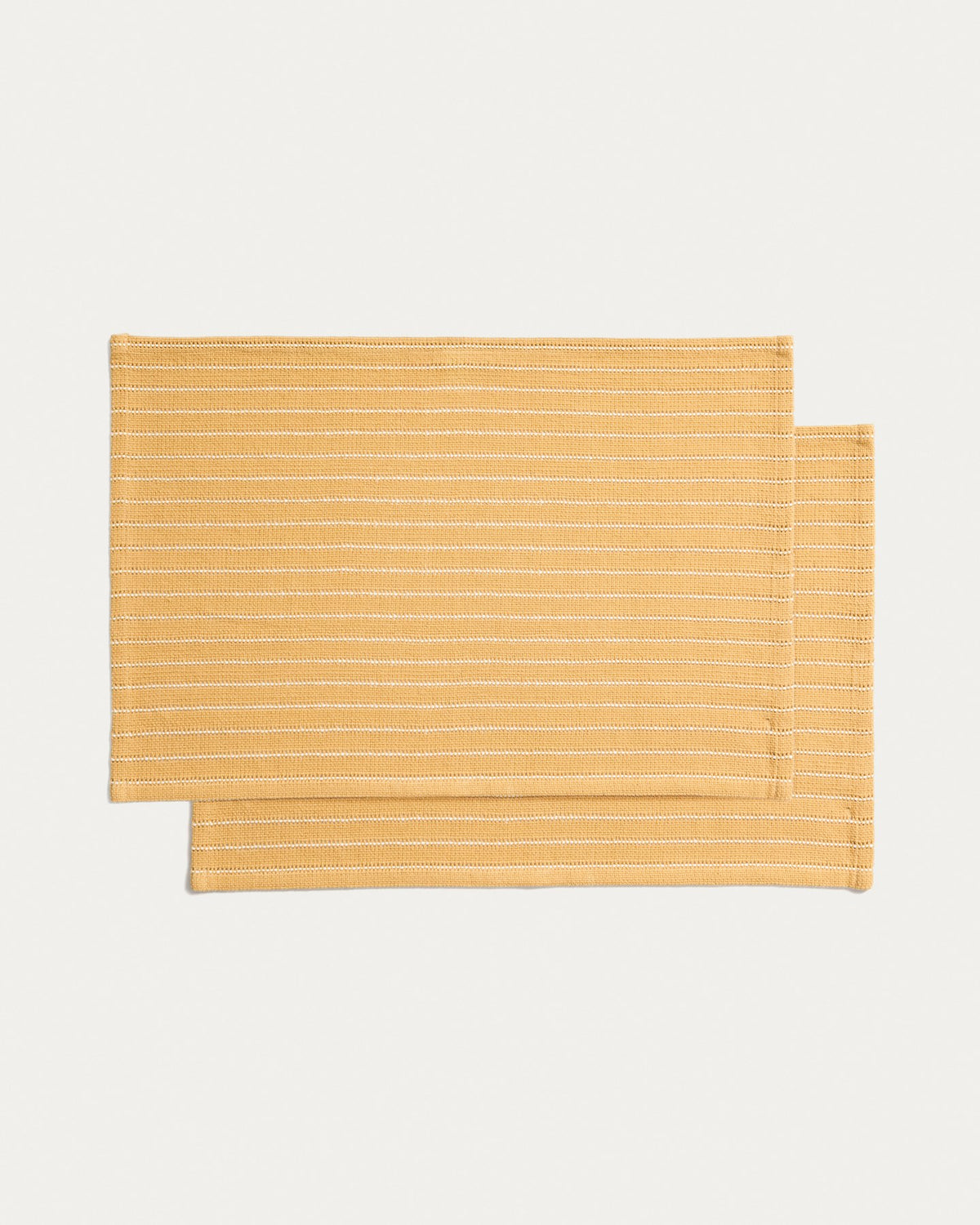 Zwei senfgelbe Tischsets aus Baumwolle mit eingewebtem Jacquard-Muster, rechteckige Form, auf einem Tisch platziert.