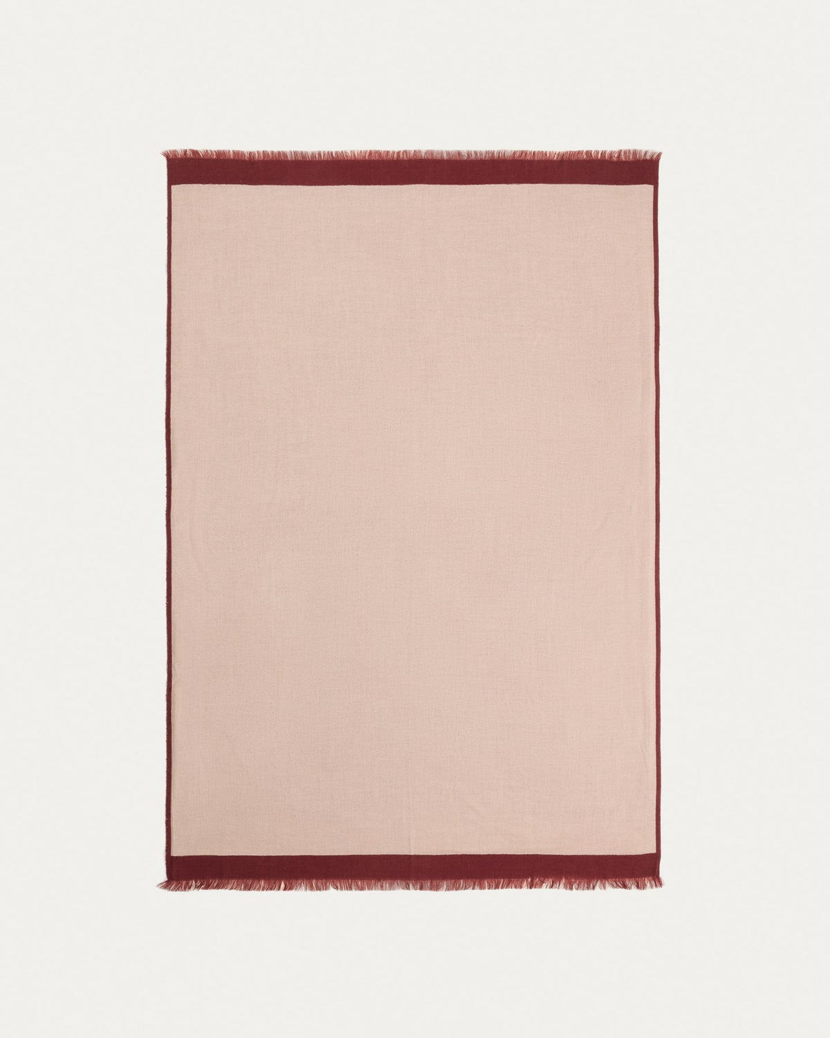 Wendbare Wolldecke aus 100% Wolle in Granatrot und Beige mit Fransen an den Rändern, gefaltet auf einem Sofa liegend.