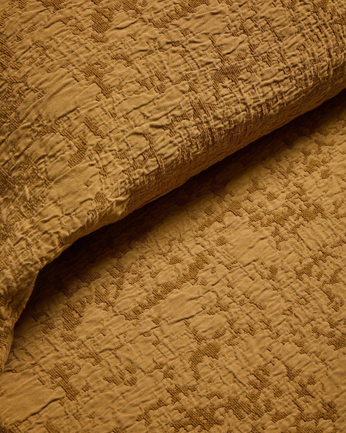 Tagesdecke Sorava von Kave Home in Senfgelb mit Jacquardmuster aus 100 % Baumwolle, drapiert auf einem 150/160-cm-Bett.