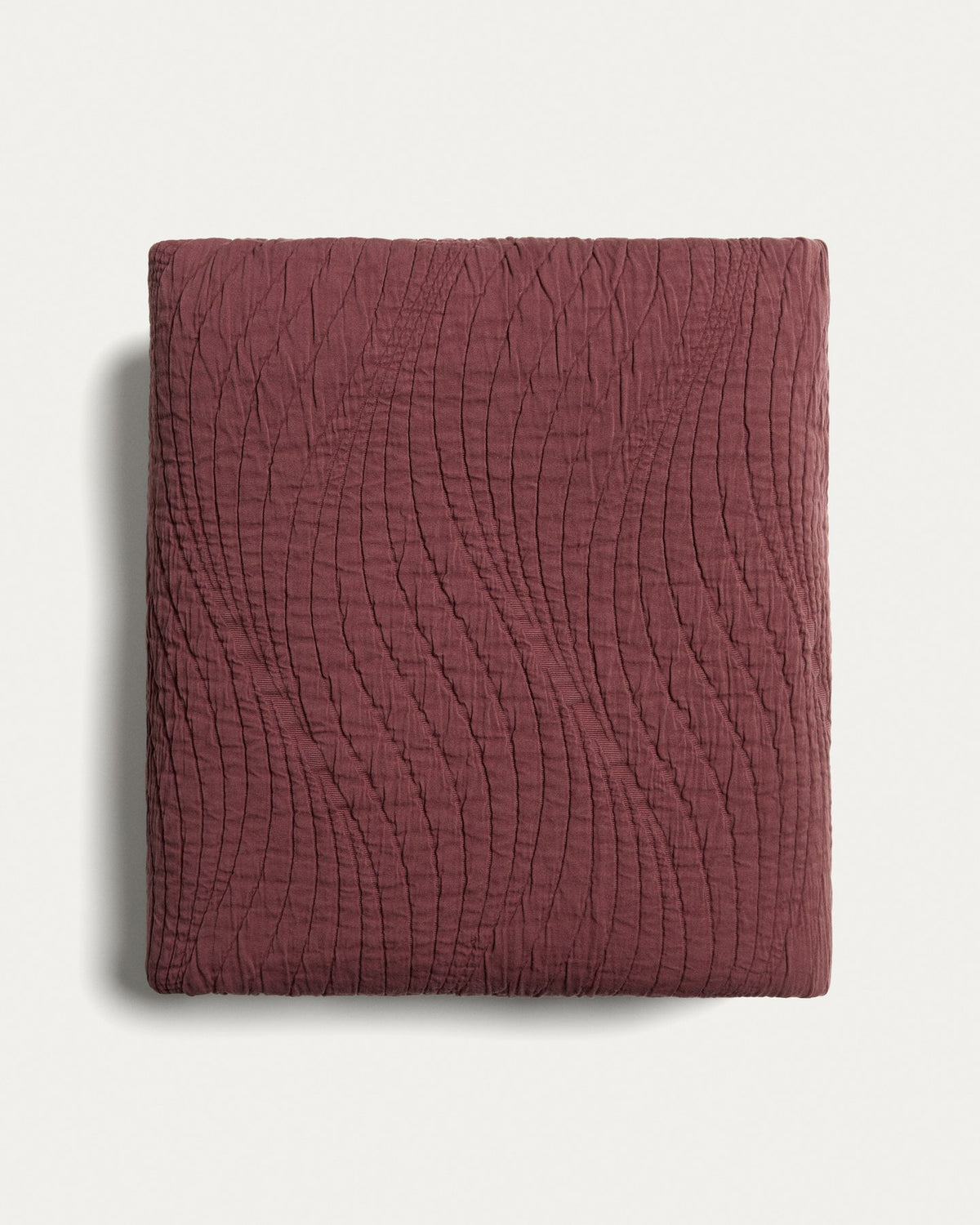 Tagesdecke Sarula aus 100% Baumwolle mit Jacquard-Wellenmuster, cremefarben, gefaltet auf einem Bett liegend, Masse 180 x 260 cm.