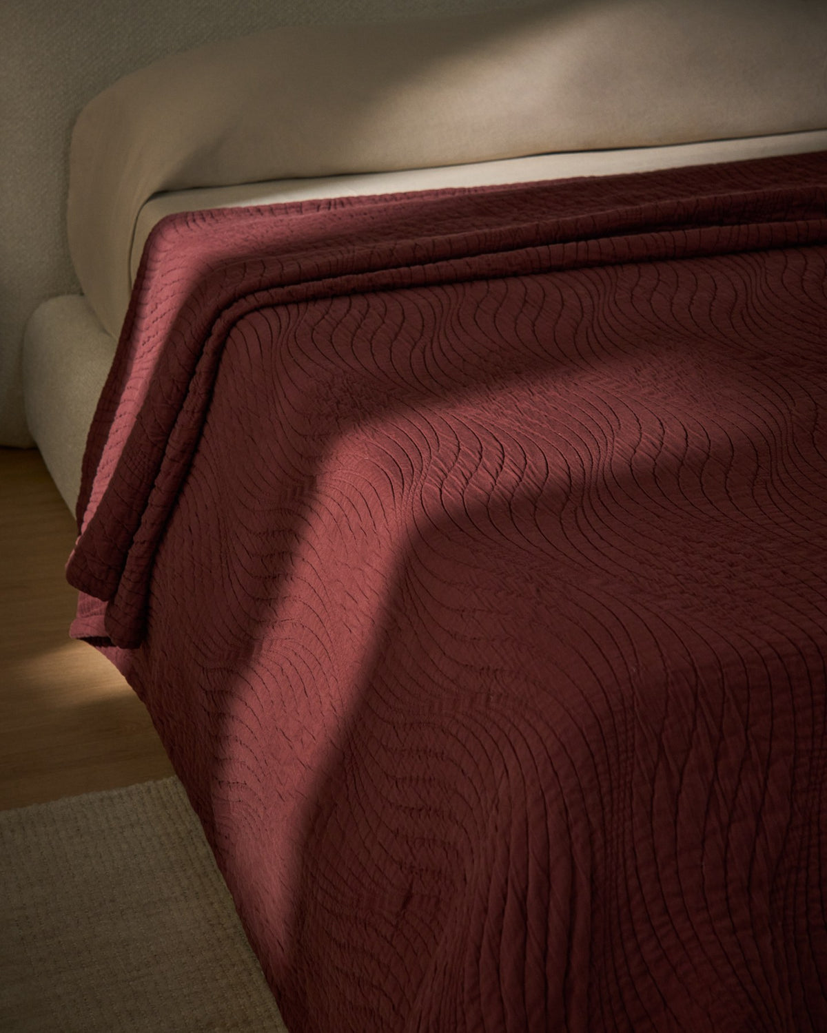 Tagesdecke Sarula aus 100% Baumwolle mit Jacquard-Wellenmuster, cremefarben, gefaltet auf einem Bett liegend, Masse 180 x 260 cm.
