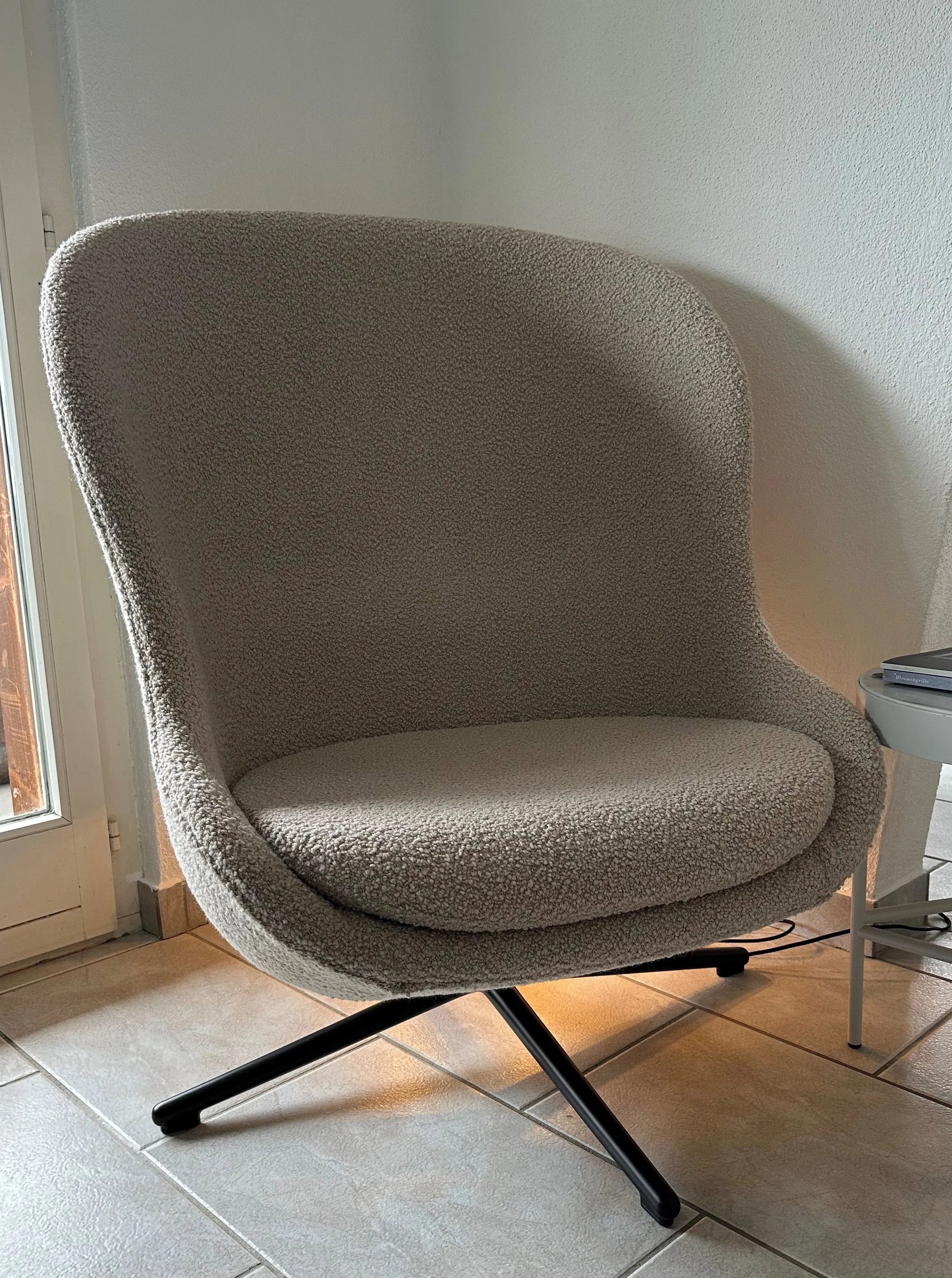 Hochwertiger Hyg Lounge Drehsessel mit hoher Rückenlehne, bezogen mit weichem Bouclé-Stoff, skandinavisches Design, drehbar und mit Neigefunktion, präsentiert als Ausstellungsstück in hellem Farbton.