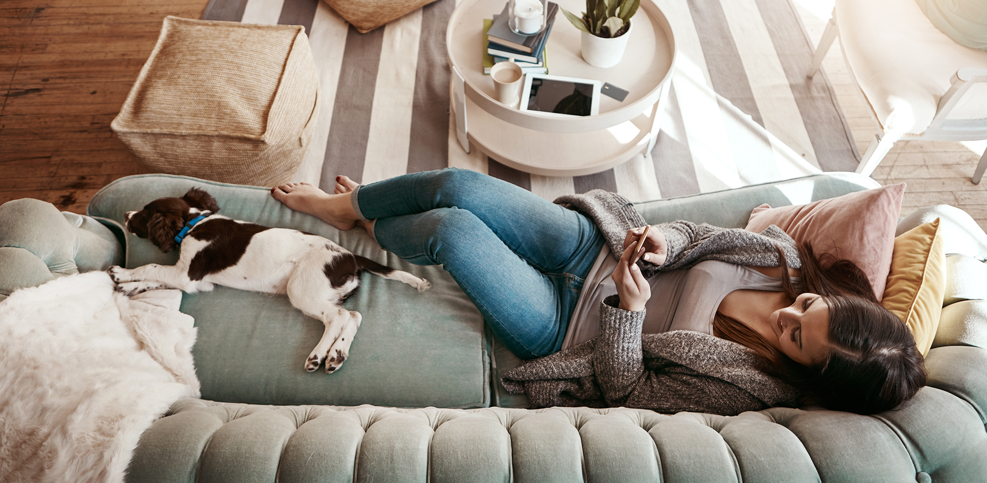 Glückliche Frau liegt mit dem Hund auf dem Sofa am Handy